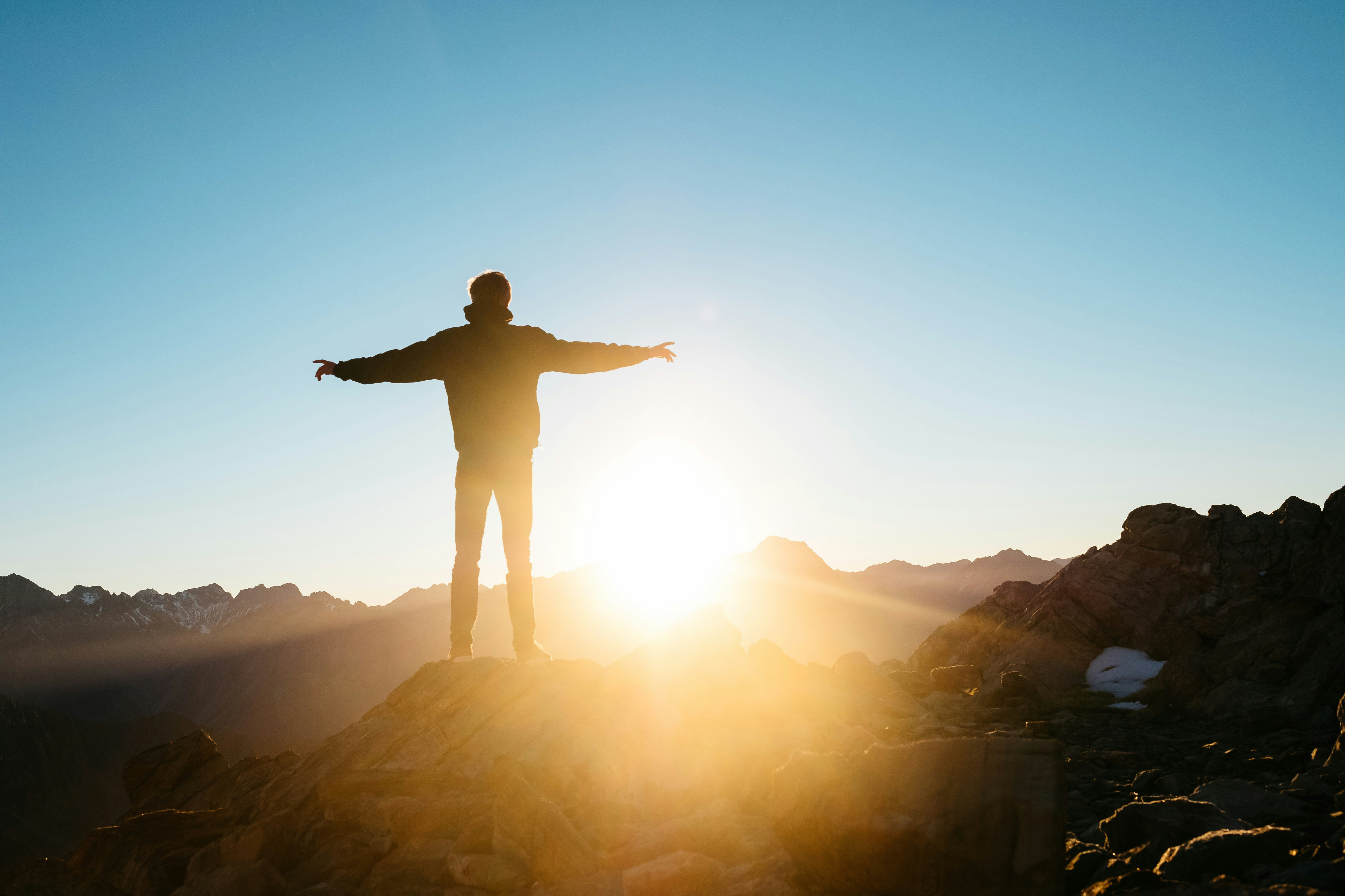 Person mit ausgebreiteten Armen auf einem Berggipfel im Sonnenaufgang